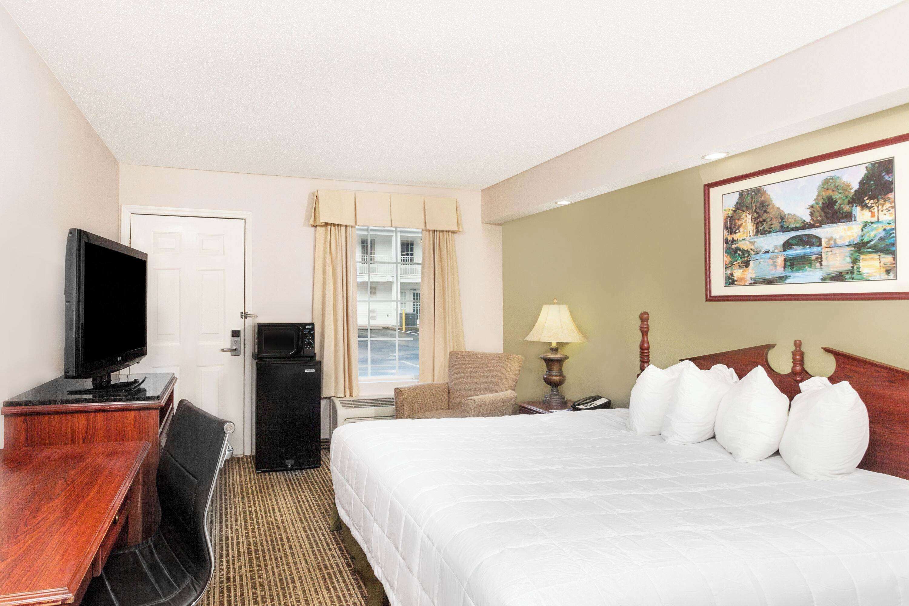 Une chambre d’hôtel avec un lit, un bureau avec une télévision, une chaise, une lampe et un tableau au mur.