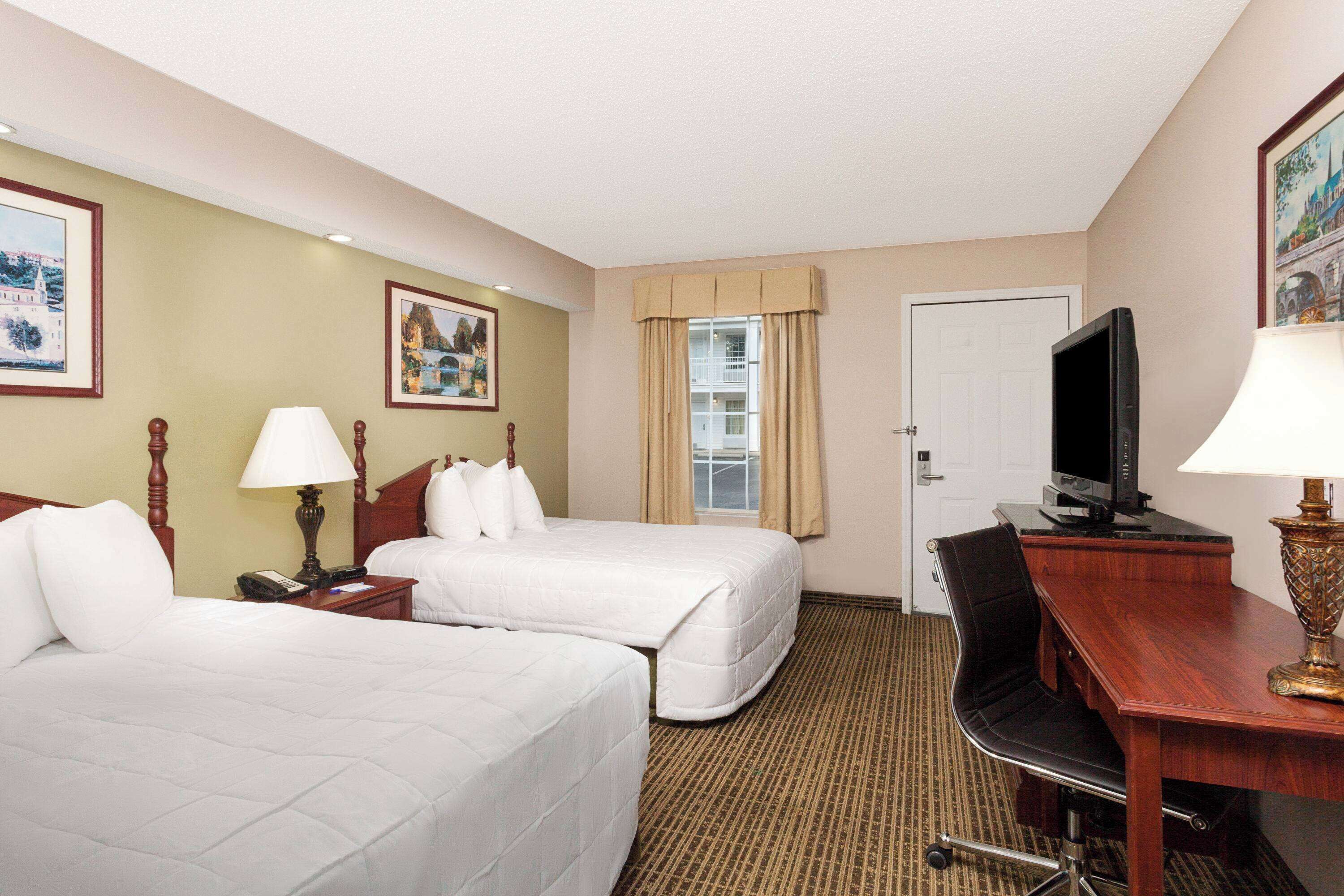 A hotel room with two beds, a desk, a television, and a chair.