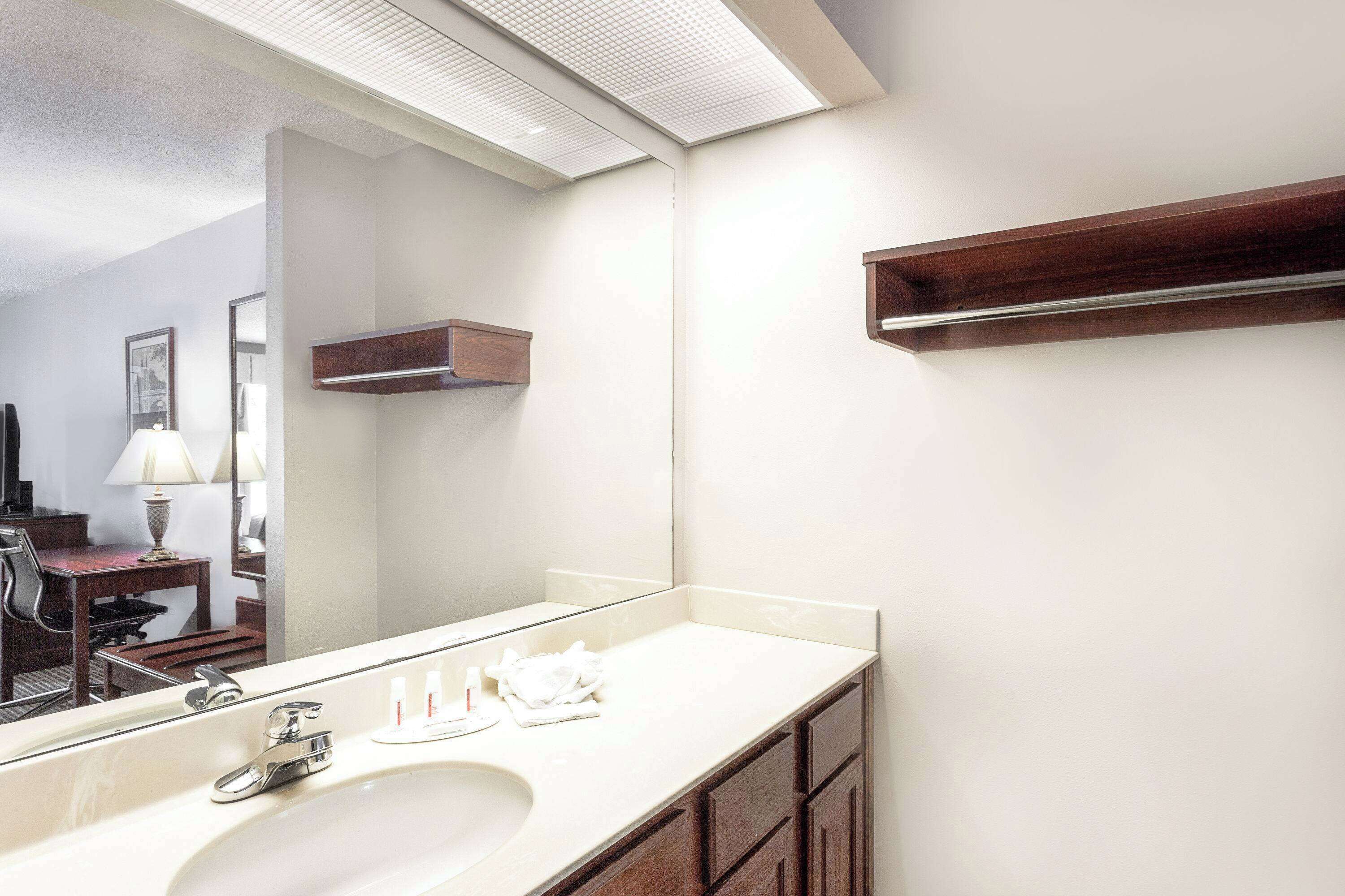 A bathroom with a large mirror, a sink, and a wooden shelf.