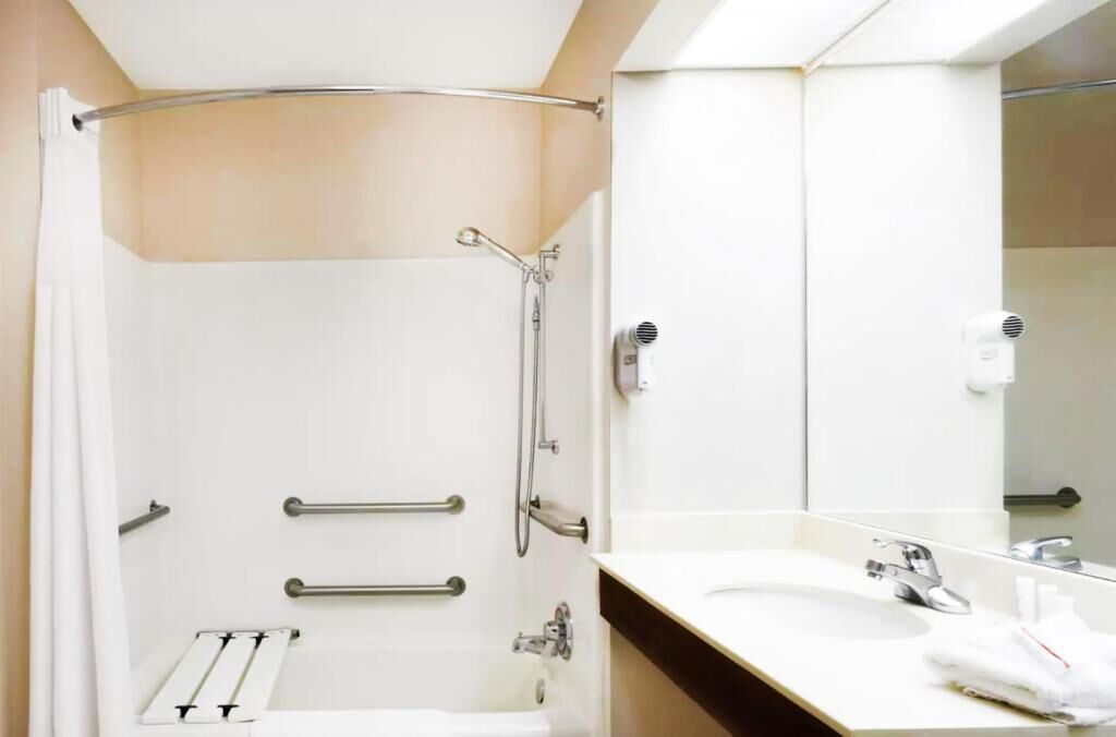 Een moderne badkamer met een douche, handgrepen, een handdoekhouder en een wastafel met spiegel.