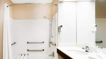 Een moderne badkamer met een douche, handgrepen, een handdoekhouder en een wastafel met spiegel.