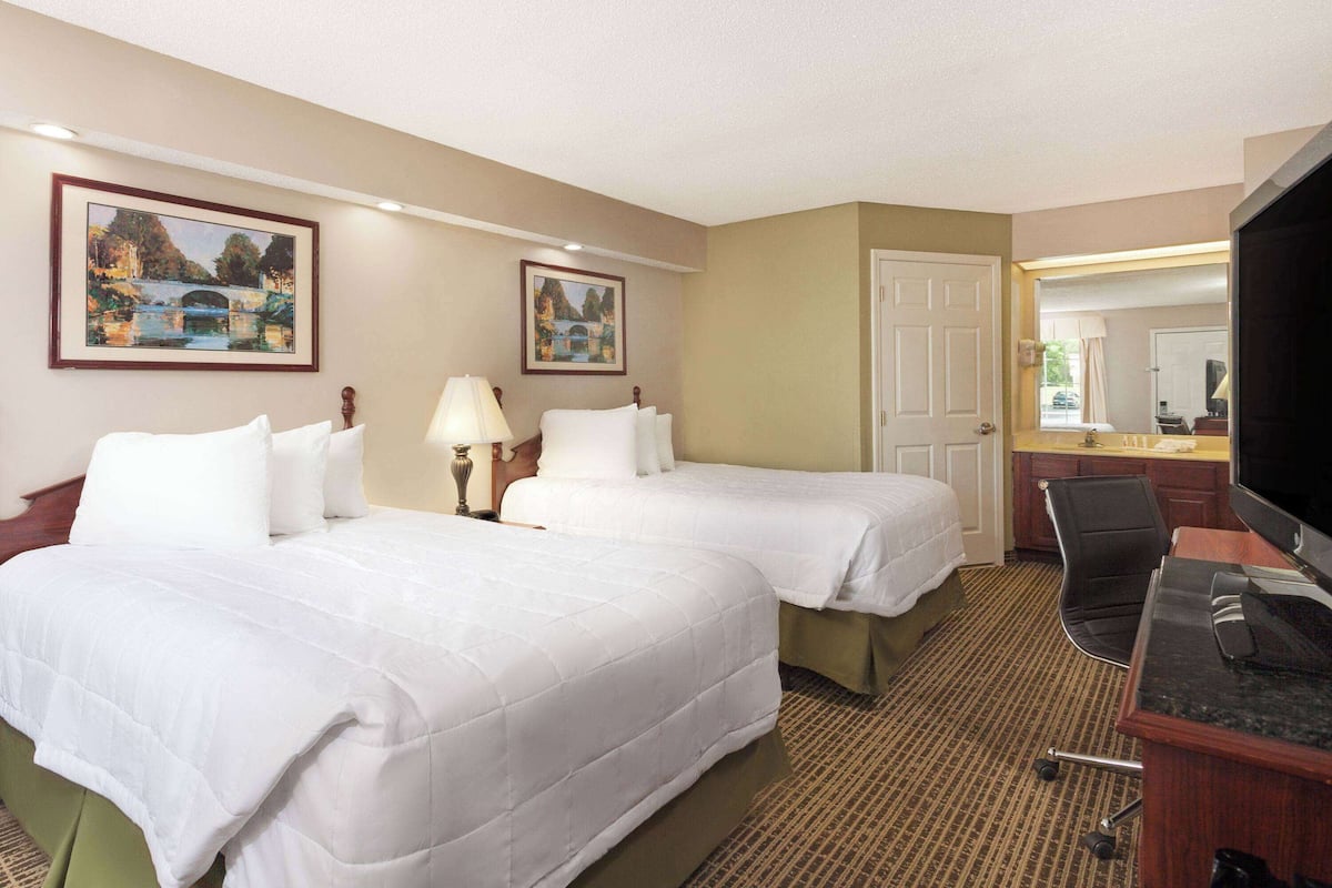 A hotel room with two beds, a desk, a chair, and a television.