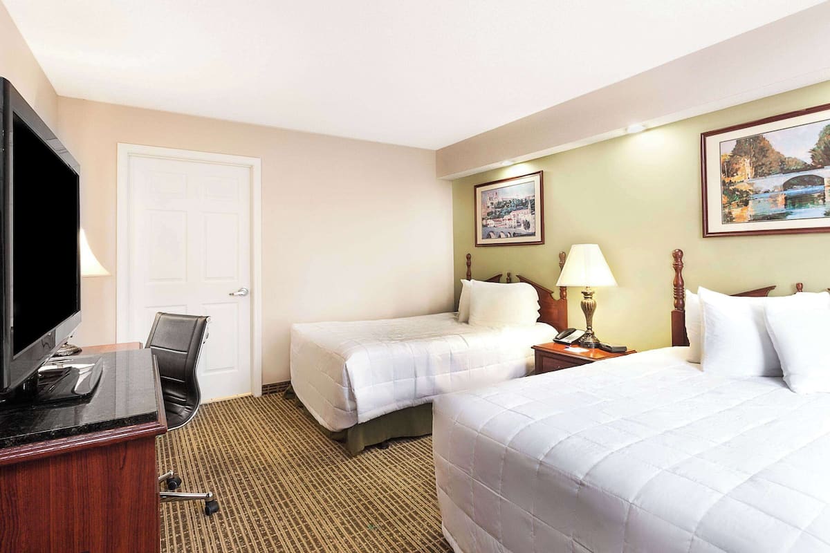 A hotel room with two beds, a desk with a computer, a television, and a lamp.