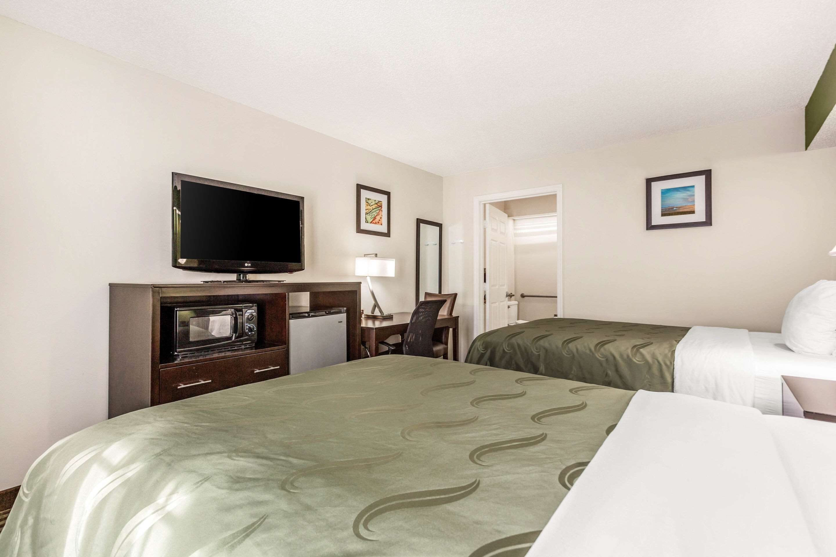 A hotel room with a bed, a desk with a computer, a television, and a microwave.