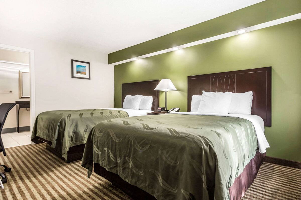 A hotel room with two beds, a desk, and a chair.