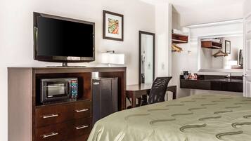 Habitación de hotel con cama, televisión, microondas, escritorio y espejo.
