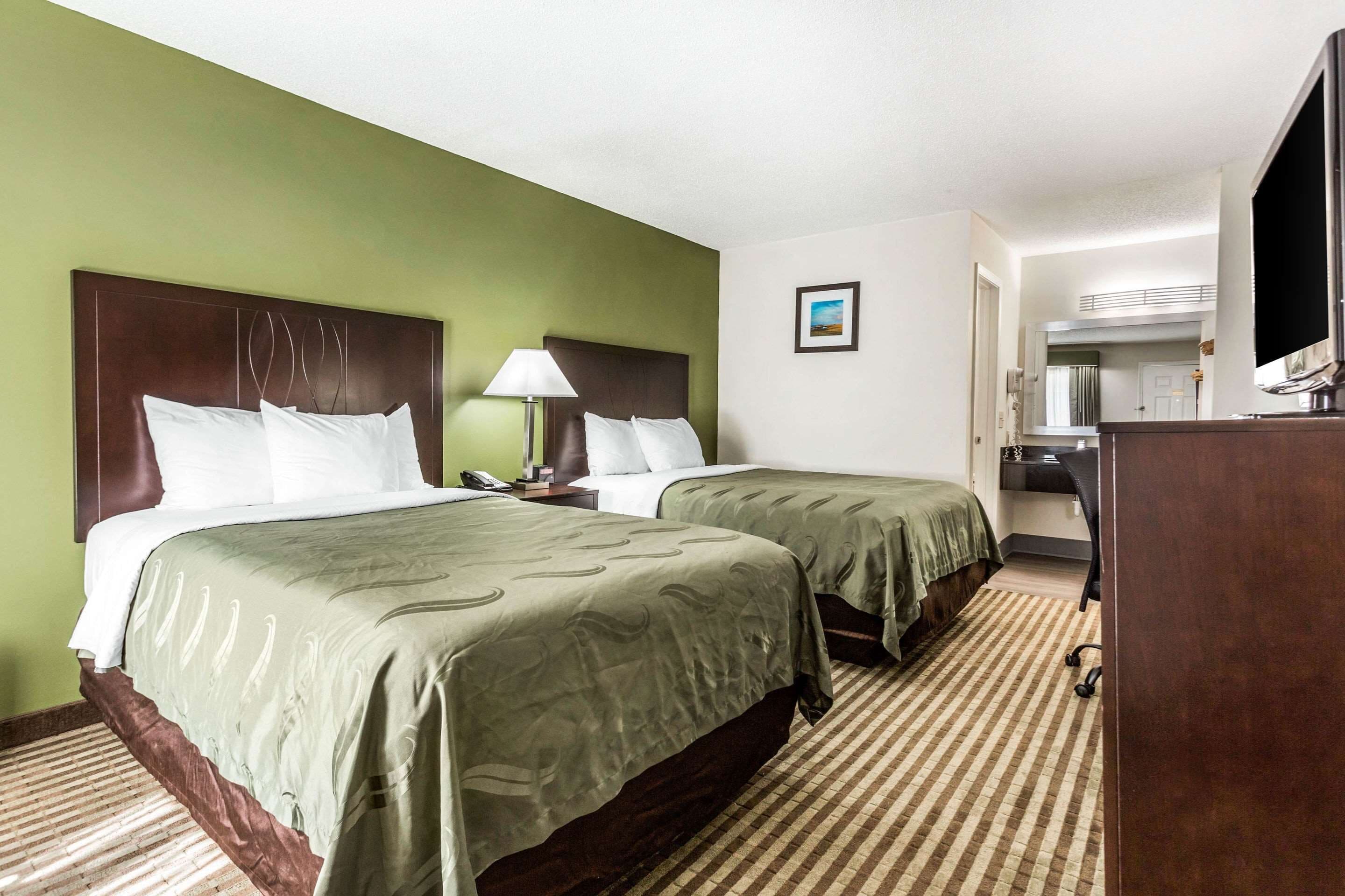 A hotel room with two beds, a desk, a chair, a TV, and a bathroom visible through an open door.