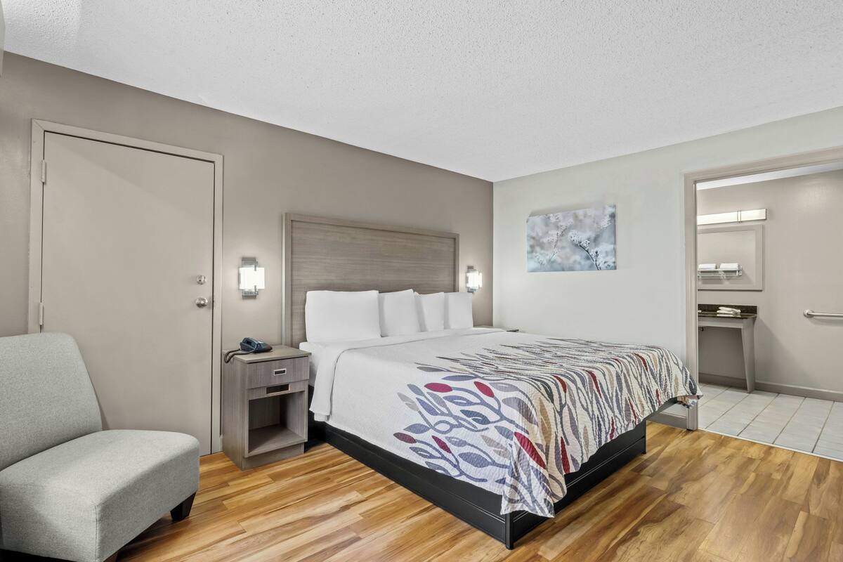 A hotel room with a bed, a chair, a nightstand, a desk, and a mirror.