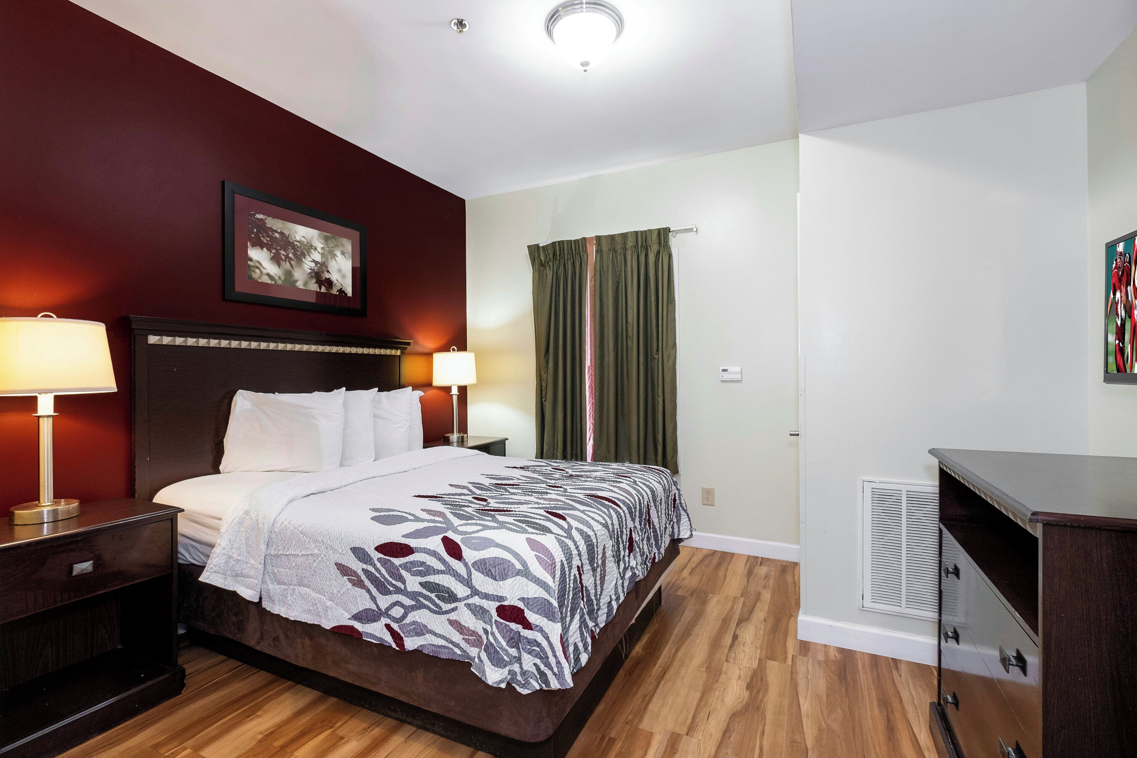 A hotel room with a bed, nightstands, a desk, a lamp, a picture on the wall, and a window with curtains.