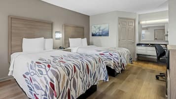 A hotel room with two beds, a desk, a chair, a mirror, and a door.