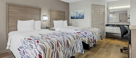 A hotel room with two beds, a desk, a chair, a mirror, and a door.