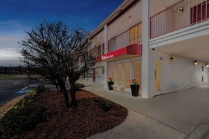 Un hotel con un toldo rojo, un árbol y una acera.