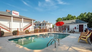A swimming pool with a red umbrella, a Red Roof Inn sign, and a fenced area with lounge chairs.