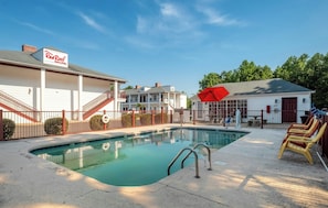 A swimming pool with a red umbrella, a Red Roof Inn sign, and a fenced area with lounge chairs. - Red Roof Inn & Suites Wilson (Wilson)