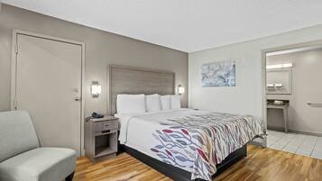 A hotel room with a bed, a chair, a nightstand, a desk, and a mirror.
