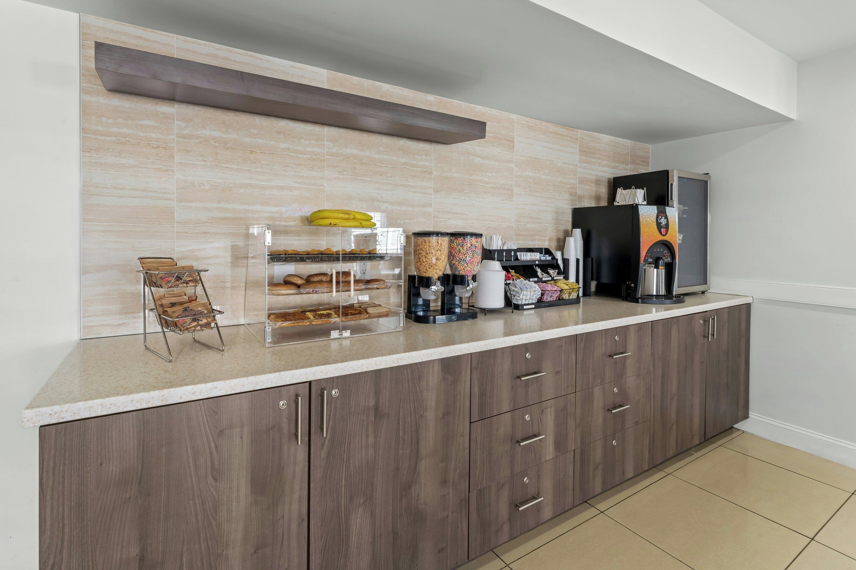 A kitchen with a countertop, a coffee machine, a refrigerator, and a shelf with snacks.