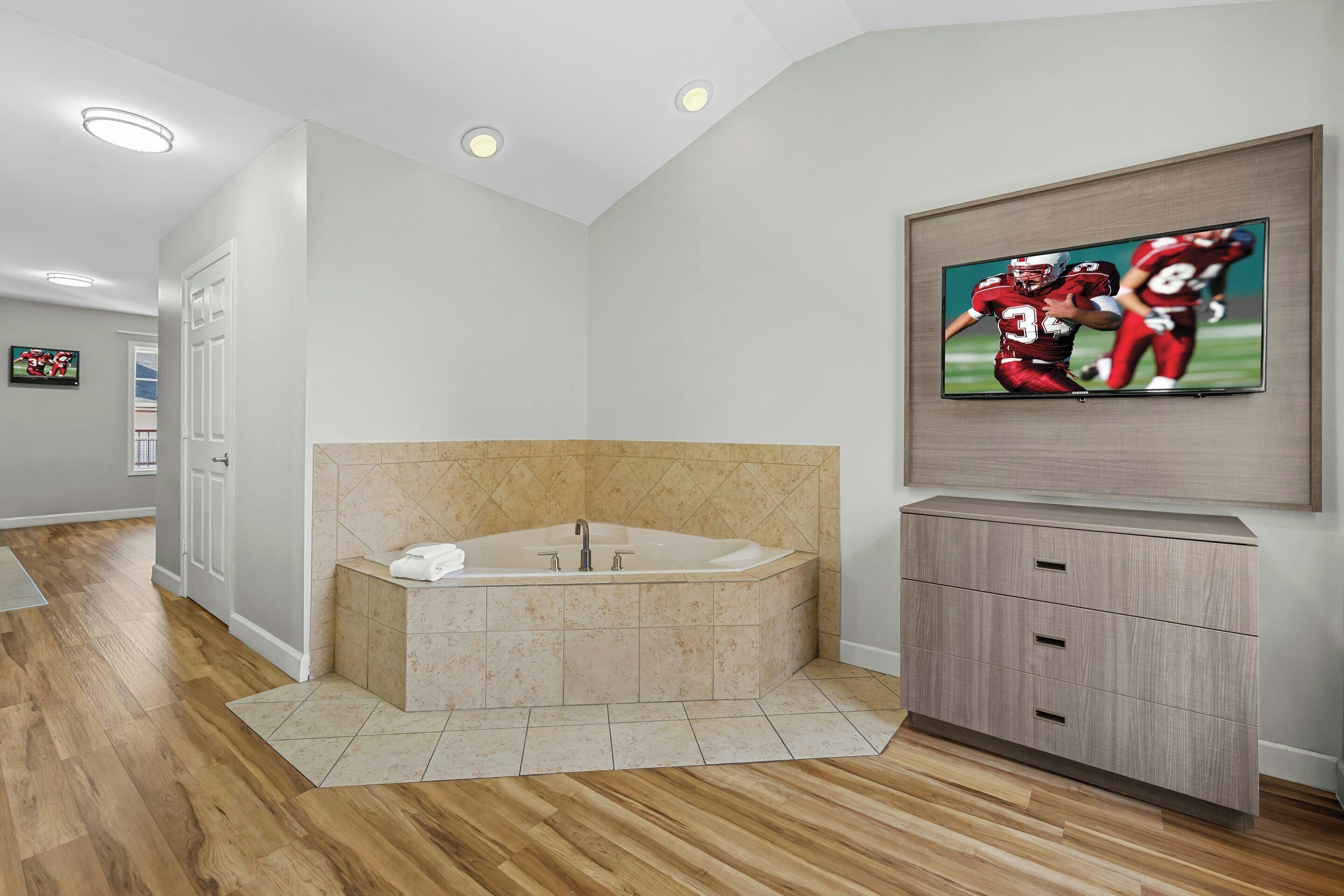 A modern bathroom with a freestanding bathtub, a vanity with drawers, and a flat-screen TV mounted on the wall.
