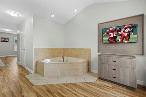 Un baño moderno con una bañera independiente, un mueble de tocador con cajones y un televisor de pantalla plana montado en la pared.