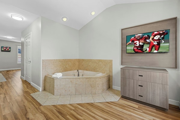 A modern bathroom with a freestanding bathtub, a vanity with drawers, and a flat-screen TV mounted on the wall.