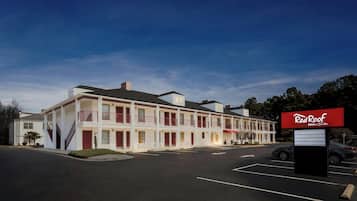 A motel with a red roof sign, multiple balconies, and a parking lot.