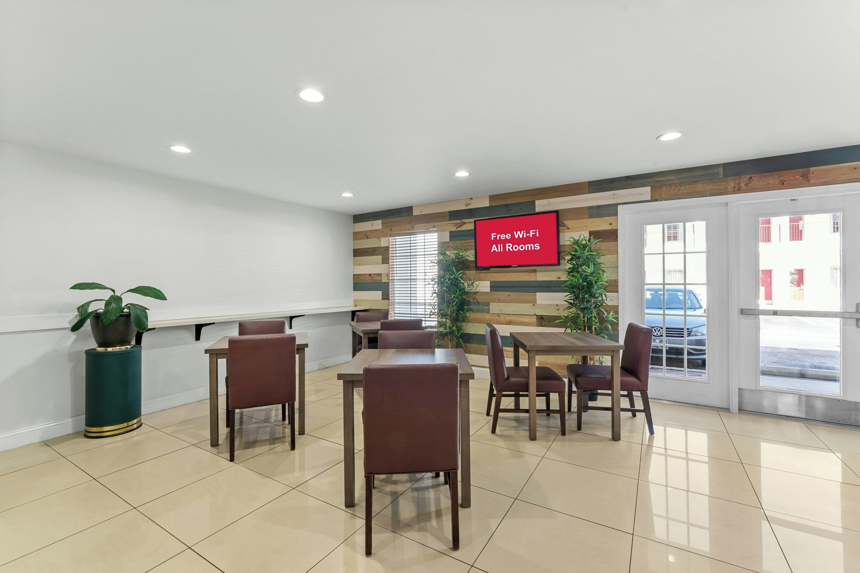 Un salón de conferencias con una pantalla grande que muestra 'Wi-Fi gratis en todas las habitaciones', un panel de pared de madera y vistas a la calle a través de la puerta.