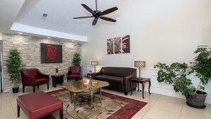 A spacious living area with a ceiling fan, a stone wall, a Red Roof Inn sign, a large sofa, a coffee table, and potted plants.