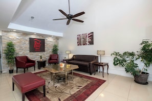 A spacious living area with a ceiling fan, a stone wall, a Red Roof Inn sign, a large sofa, a coffee table, and potted plants. - Red Roof Inn & Suites Wilson (Wilson)