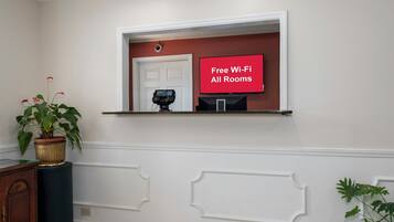 A room with a white wall, a door, a mounted television, and a potted plant.