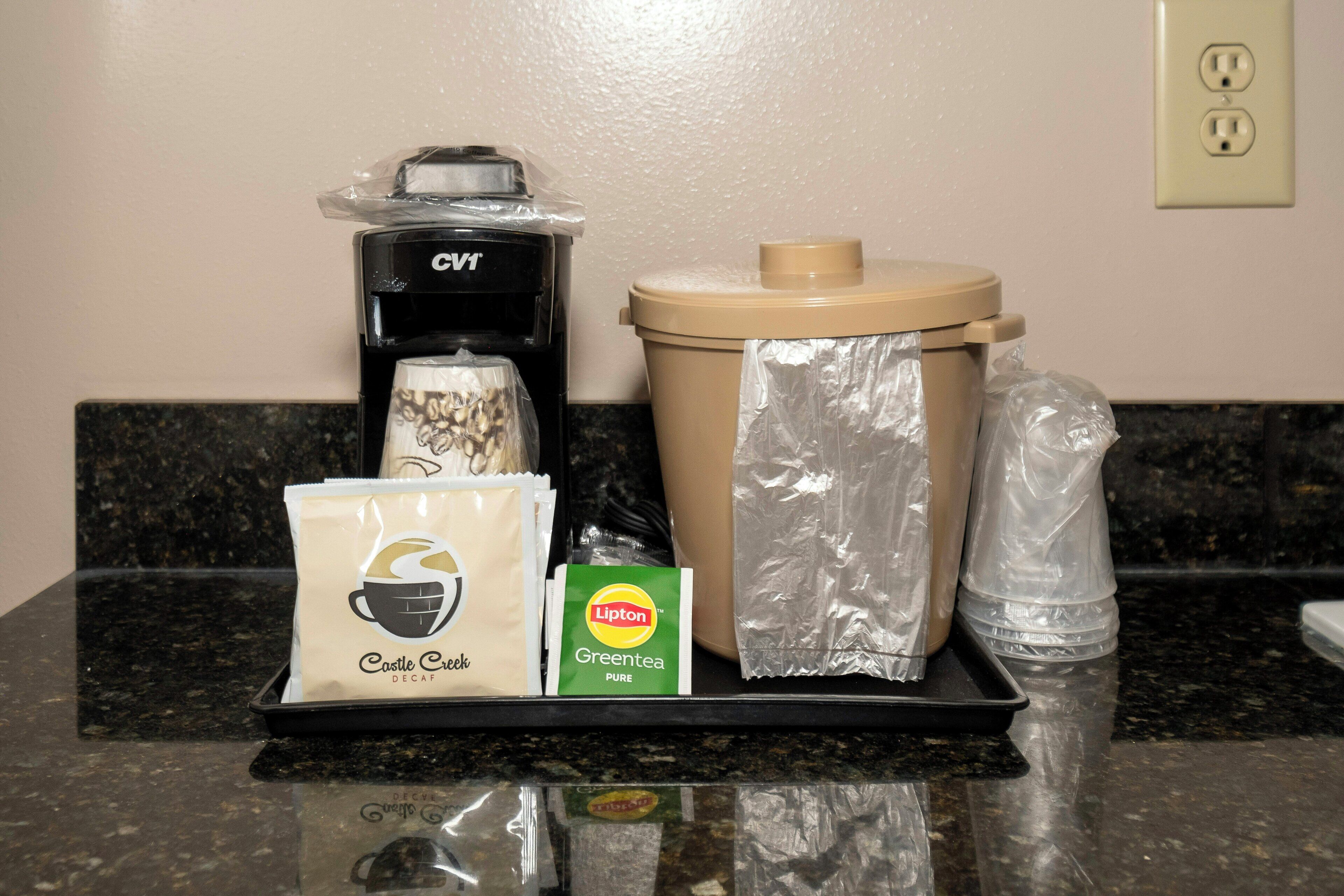 A coffee maker, a trash can, a bag of Castle Creek decaf coffee, a packet of Lipton green tea, and a bag of Lipton green tea.