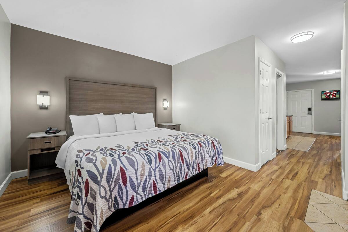 A bedroom with a wooden floor, a bed with a patterned bedspread, bedside lamps, and a nightstand.