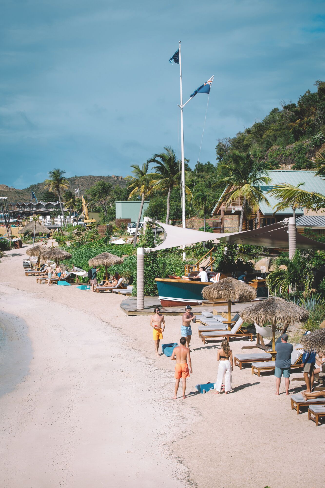 A beachside resort with sun loungers, a boat, and a thatched-roof structure.