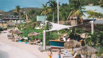 A beachside resort with sun loungers, a boat, and a thatched-roof structure.