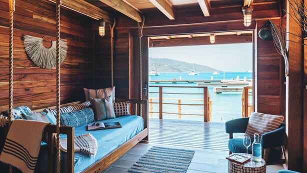 Eine Holzhütte mit Bett, Stuhl und Blick auf das Meer.