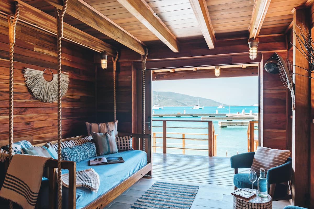 Eine Holzhütte mit Bett, Stuhl und Blick auf das Meer.
