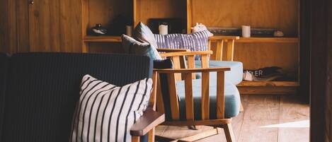Una sala de estar acogedora con piso de madera, un sofá a rayas, una silla de madera y una estantería.