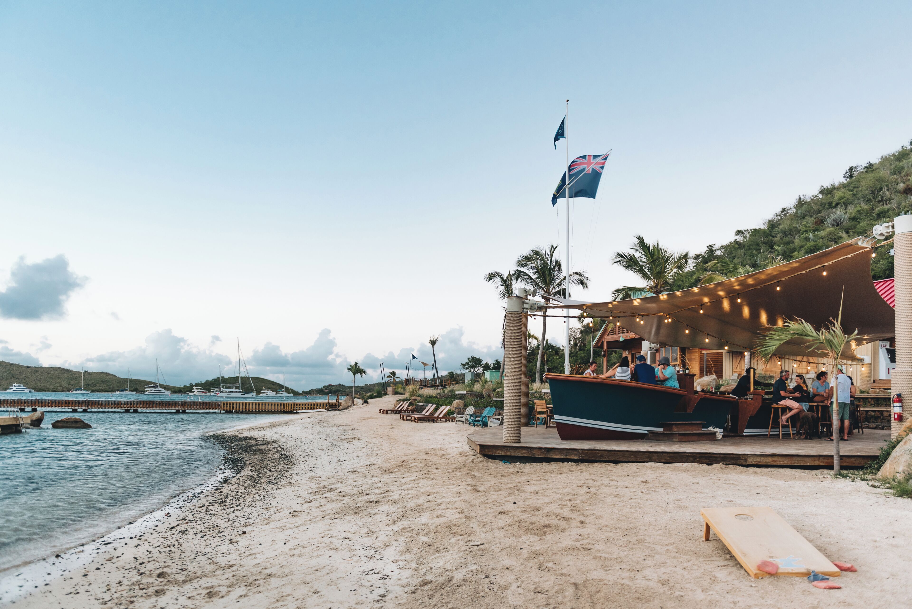Un bar en la playa con terraza, una bandera y un bote.