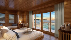 Ein Holzhüttenraum mit einem Bett, einem Sessel, einer Lampe und Blick auf das Meer.
