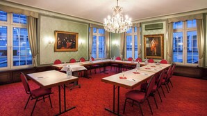 Un salón de conferencias con alfombra roja, ventanas amplias y cuadros en las paredes.