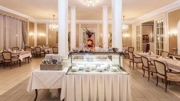 Un comedor formal con varias mesas, un bufé con diversos platillos y elegantes candelabros.