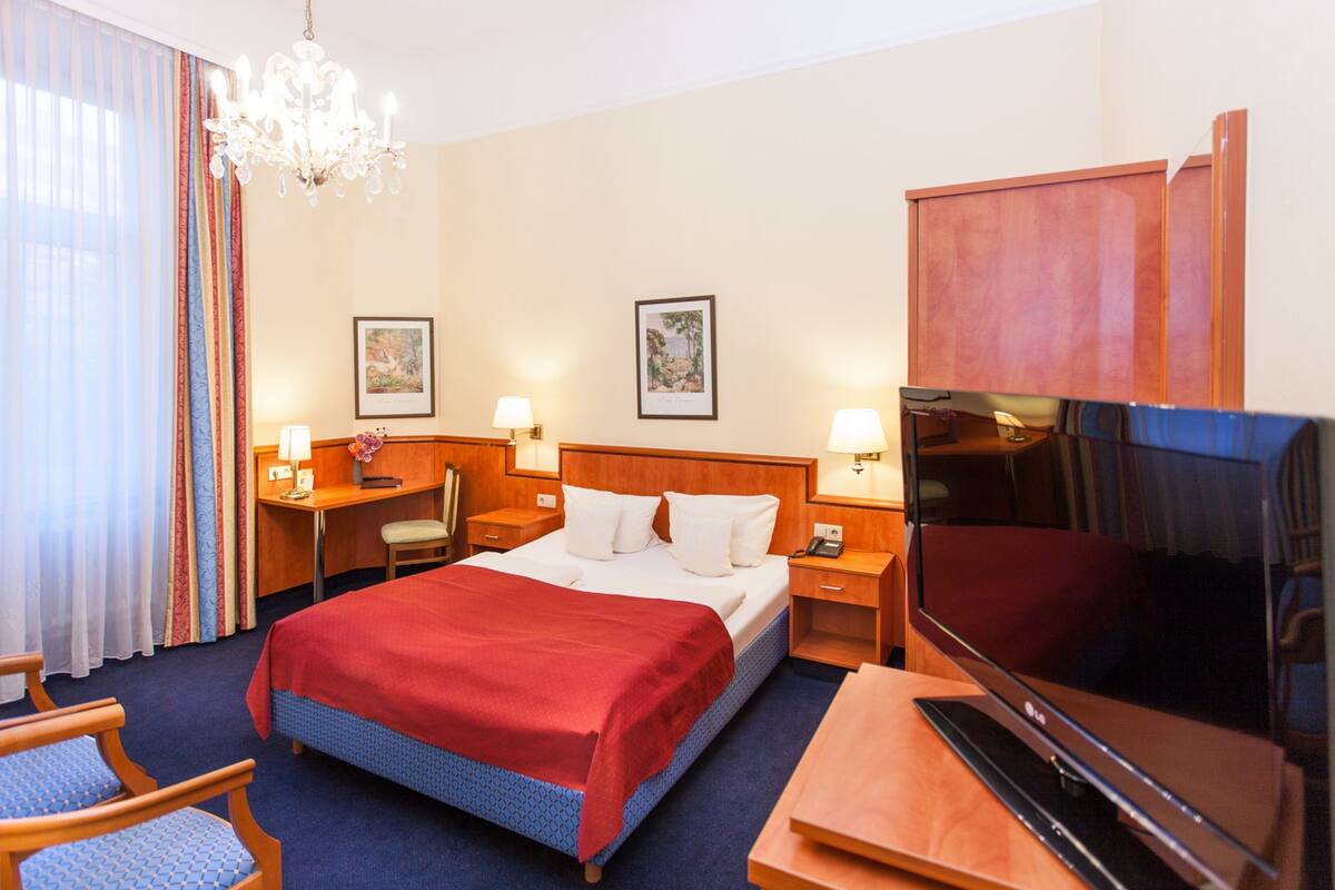 Ein Hotelzimmer mit Bett, Schreibtisch, Stuhl, Fernseher und Bildern an den Wänden.