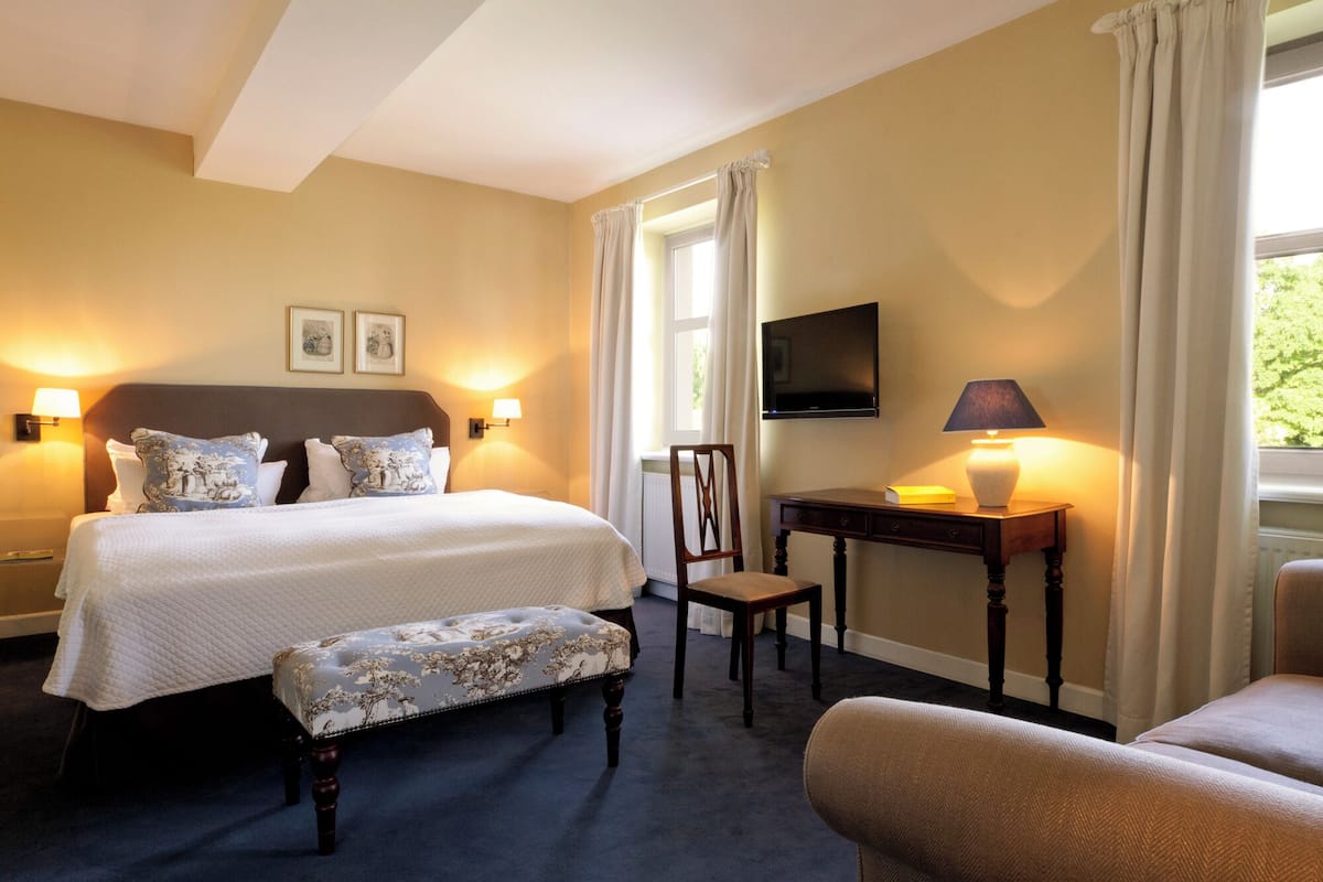 A hotel room with a large bed, a desk with a lamp, a chair, and a television on the wall.