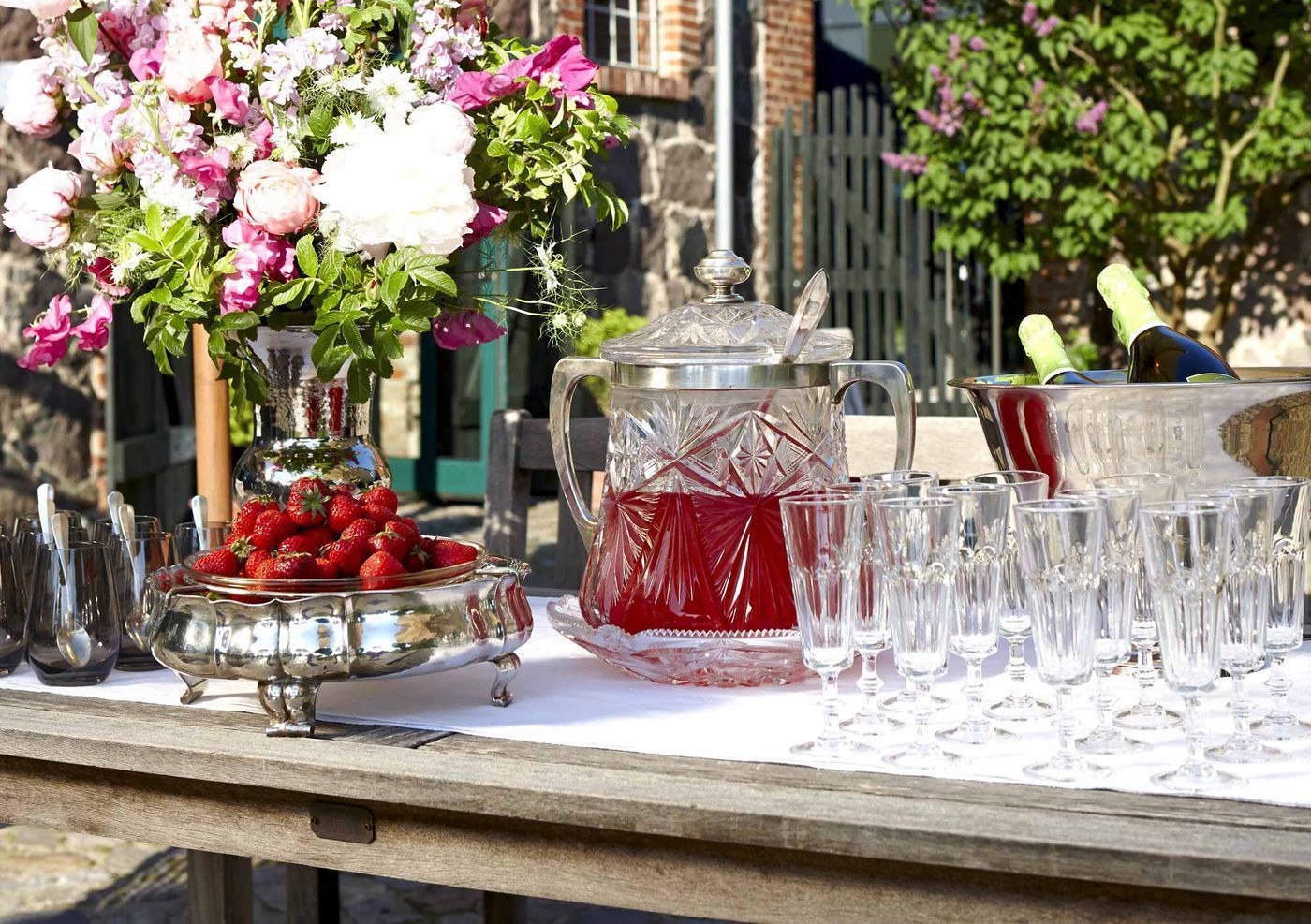 A table with a fruit bowl, a pitcher, and multiple glasses, suggesting a refreshment setup.