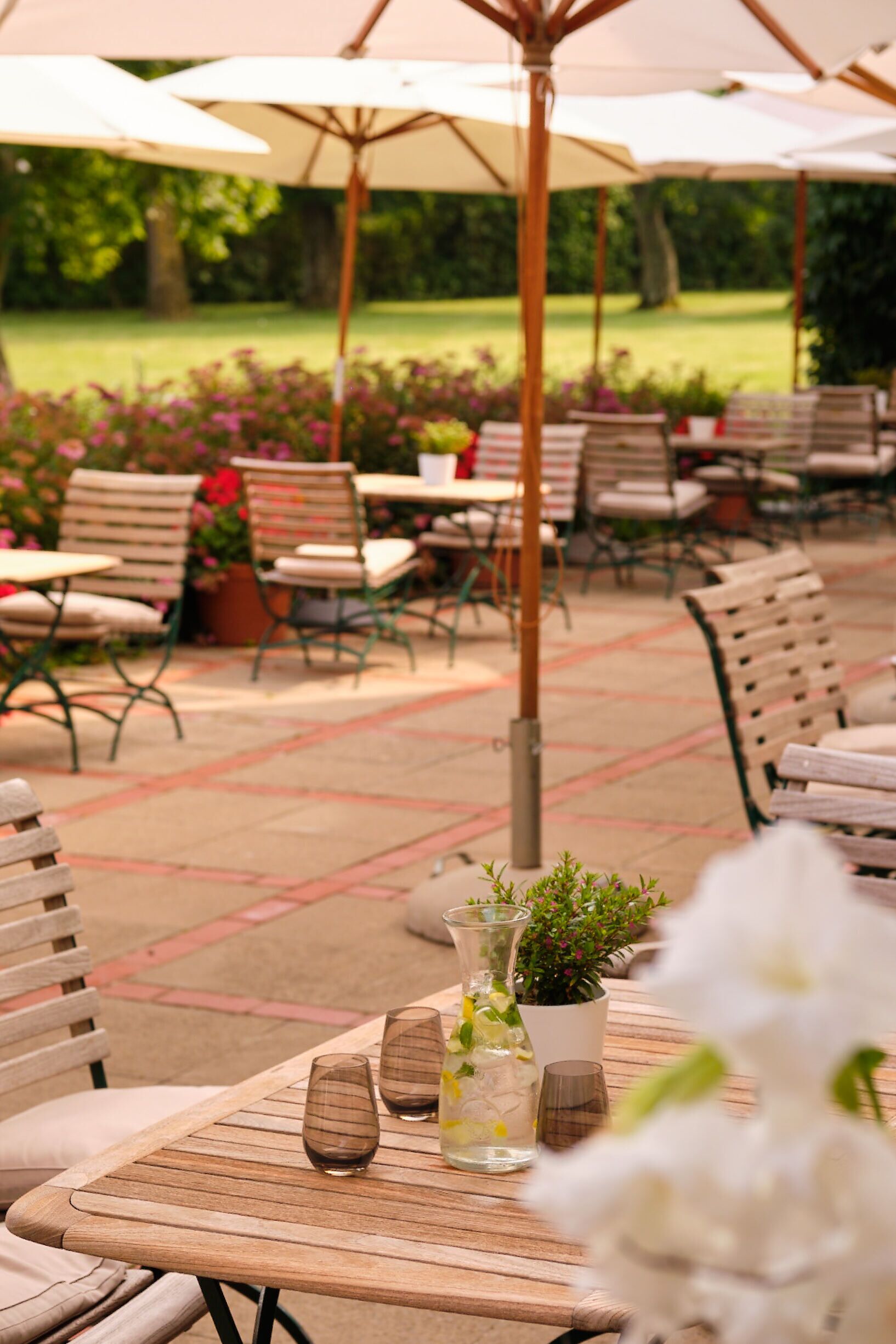 An outdoor patio with wooden tables and chairs, umbrellas, and potted plants.