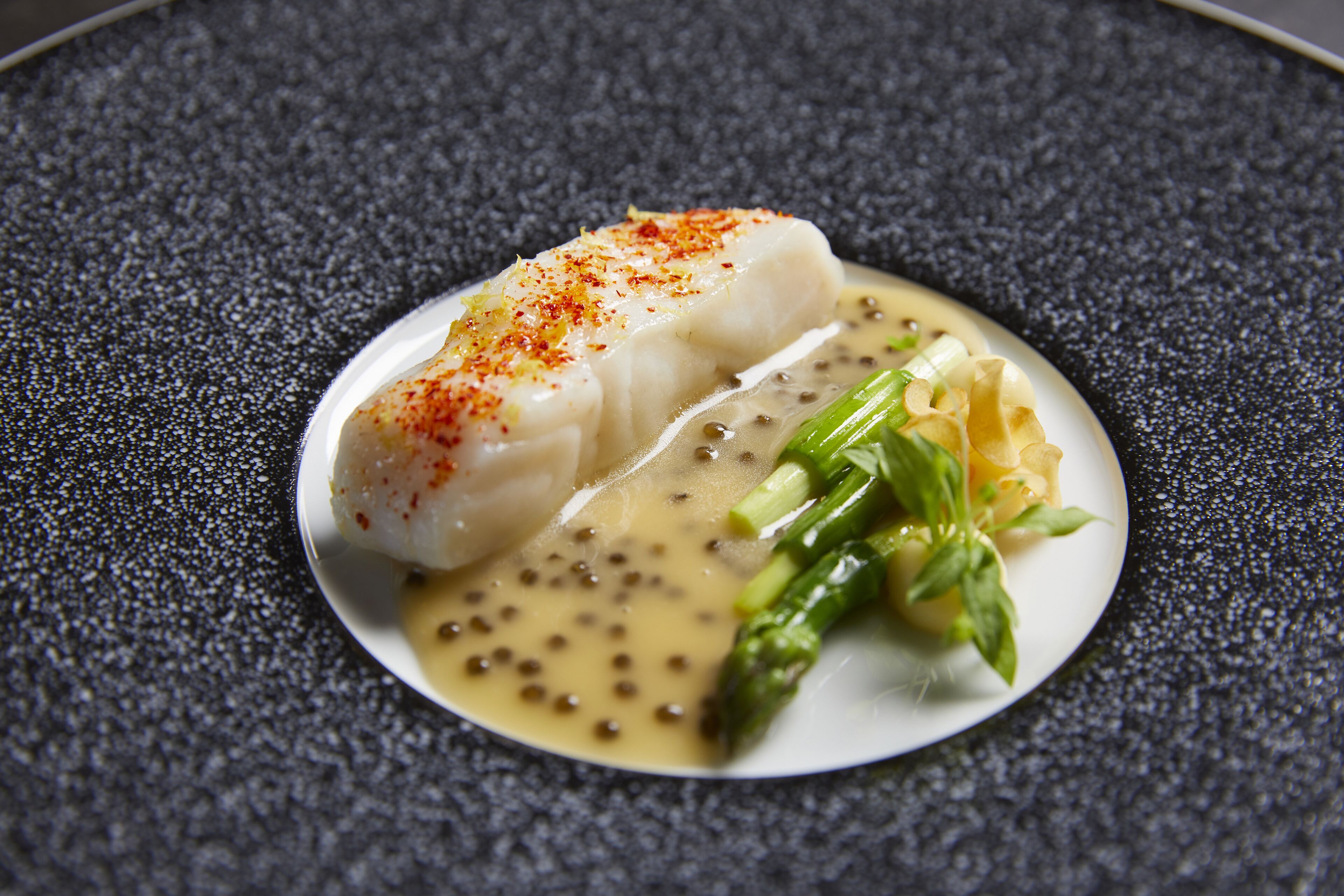 A plate of food with fish, asparagus, and a creamy sauce.