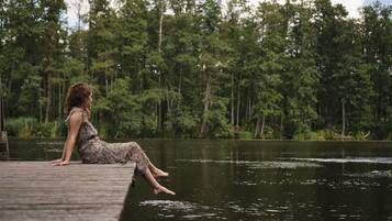 A person sitting on a wooden dock by a lake with a forest in the background.