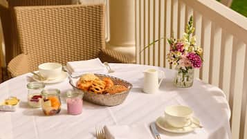A table set with white tablecloths, wicker chairs, and a wicker basket filled with snacks.