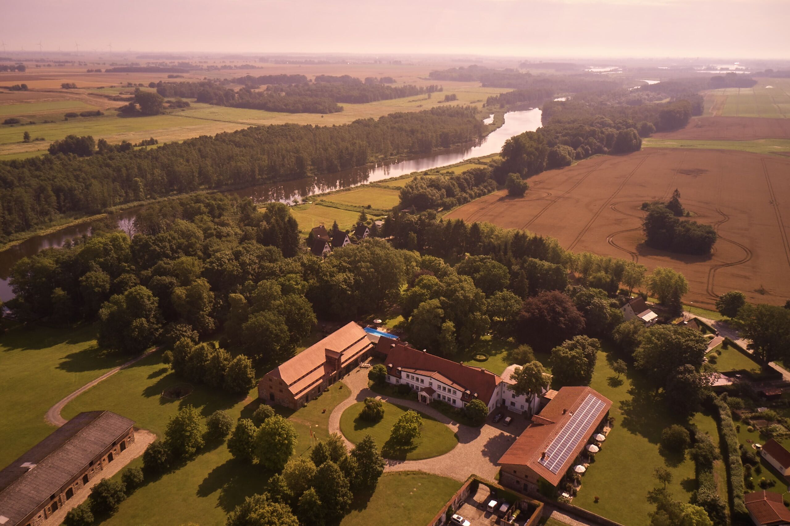 An aerial view of a large estate with multiple buildings, a river, and surrounding fields.