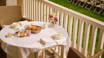 A round table with a white tablecloth, set with a basket of pastries, a pitcher, and a vase of flowers.