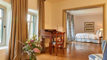 A room with a piano, a bed, a chair, and a vase of flowers.