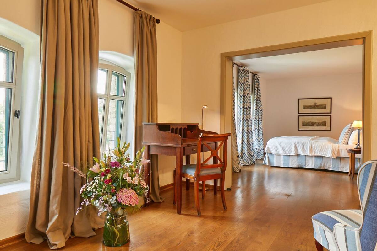 A room with a wooden desk, a chair, a bed, and a window with curtains.